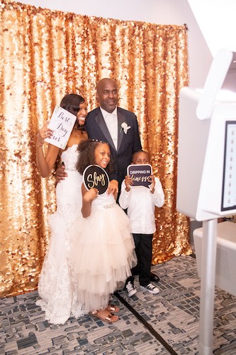 Photo booth - bride and groom taking photos with their children in a Photo Booth - photo booth with a gold backdrop - blended families