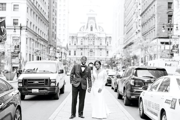 Black bride and groom posing for wedding photos on South Broad Street in front of Philadelphia's City Hall