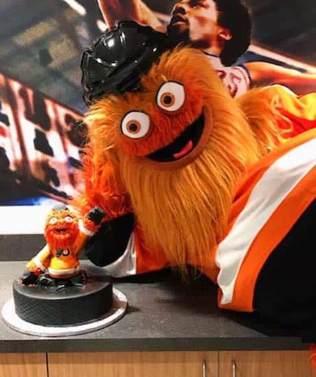 Iconic Philadelphia Flyers mascot Gritty posing in front of a Gritty themed cake by Bredenbeck's Bakery