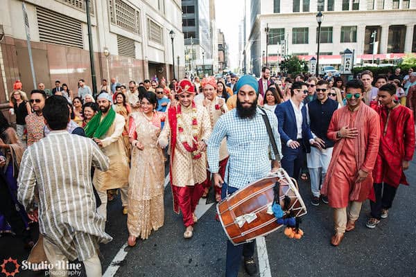 a traditional drummer and wedding guests leading a South Asian groom though the streets of Philadelphia