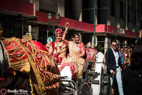 South Asian bride and groom riding in a decorated horse and carriage after their Philadelphia wedding