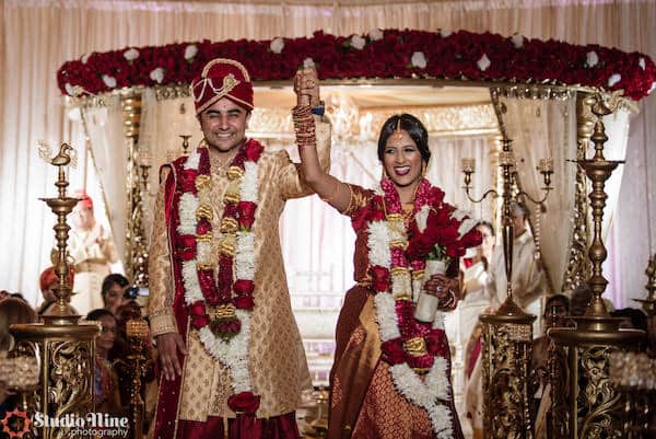 Philadelphia South Asian bride and groom standing under a gold and red mandap