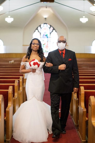 bride walking down the aisle escorted by family member wearing a mask