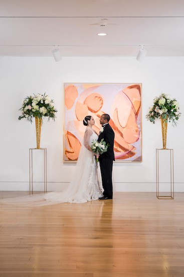 Black bride and groom standing between modern hunter green and gold arrangements at PAFA