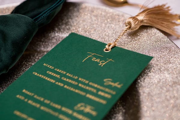 Hunter green and gold place setting with a custom menu card and velvet napkin on a gold charger plate