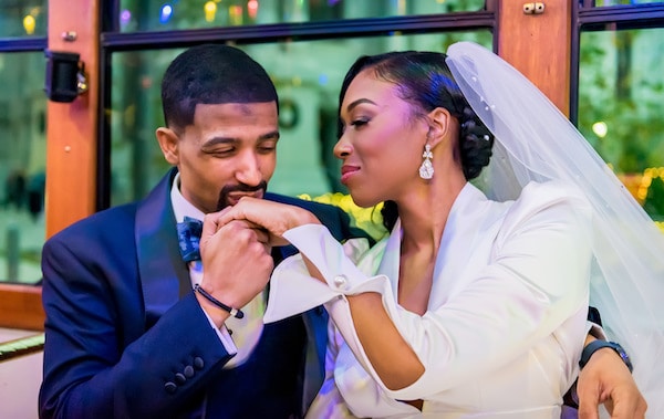 Groom kissing his bride's hand while they ride on a trolley