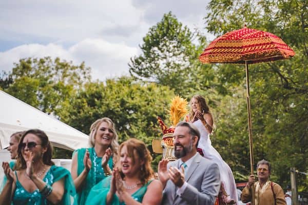 bride riding on a white horse during a baraat surrounded by family and friends