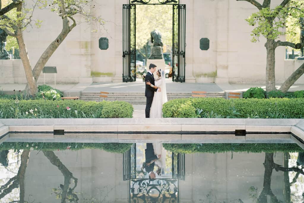 Bride and groom standing by a reflective pool at the Rodin Museum wedding venue