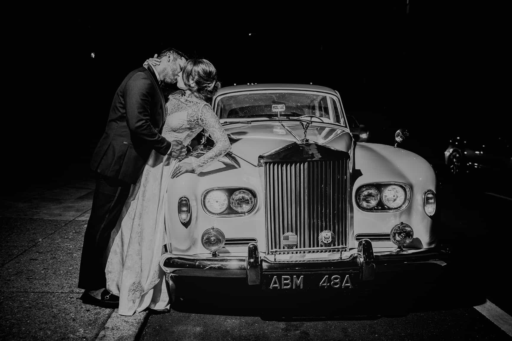 Bride and groom pose with vintage getaway car